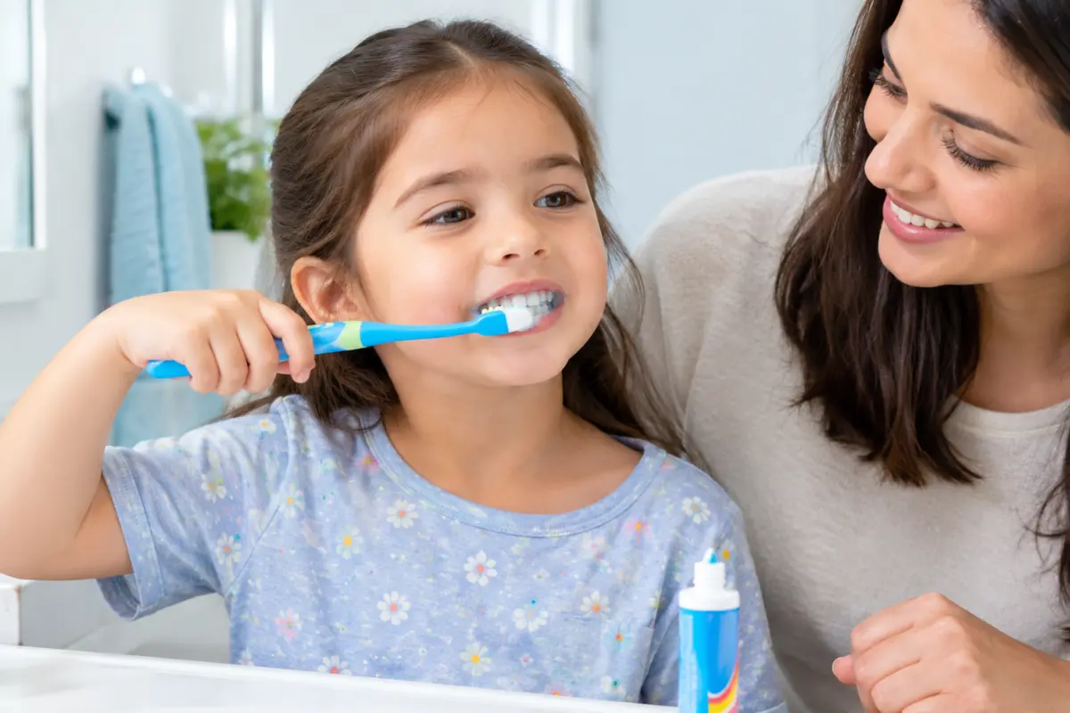 Child brushing teeth with fluoride toothpaste and parental supervision